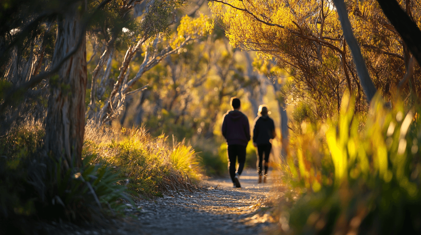 Two people walking a trail amidst lush coastal vegetation at golden hour